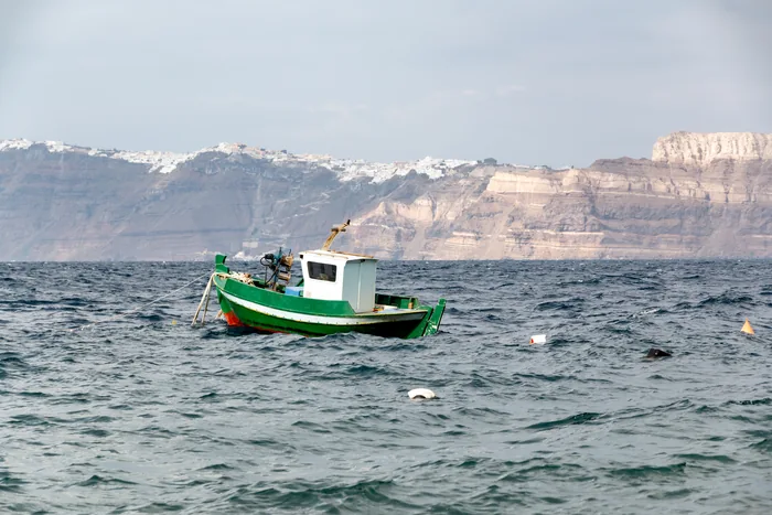 A small boat against the caldera cliffs near Akrotiri, Santorini